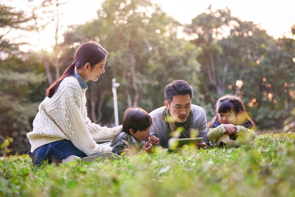 azjatycka rodzina z dwójką dzieci relaksujących się na świeżym powietrzu w parku miejskim - Zdjęcie, obraz