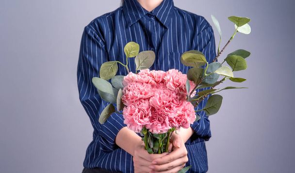 Young girl in dark blue striped shirt giving bunch of handmade beautiful blooming baby pink color carnations as a gift for mothers day concept, close up, copy space, clipping path - Фото, изображение