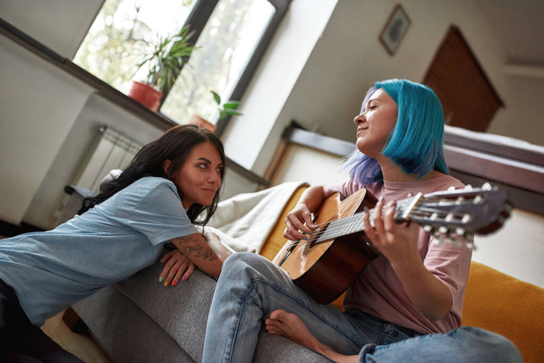Lovely lesbian couple with guitar in light living room - Φωτογραφία, εικόνα