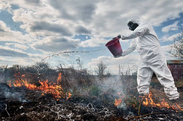 Еколог пожежник бореться з вогнем у полі з хмарним небом на фоні
 - Фото, зображення