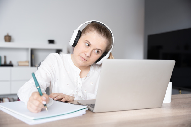 Estudante do sexo feminino tomando notas em um caderno na frente de um laptop durante uma aula virtual - Foto, Imagem