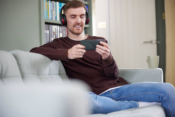 Man At Home Wearing Wireless Headphones Streaming Music Or Film From Mobile Phone - Photo, Image