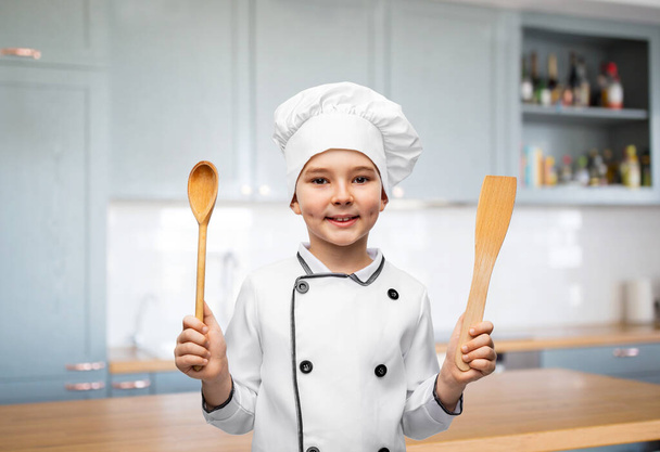 glimlachende jongen in koks toque met lepel en spatel - Foto, afbeelding