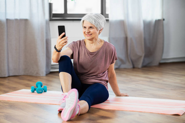 senior woman with smartphone exercising at home - Fotografie, Obrázek