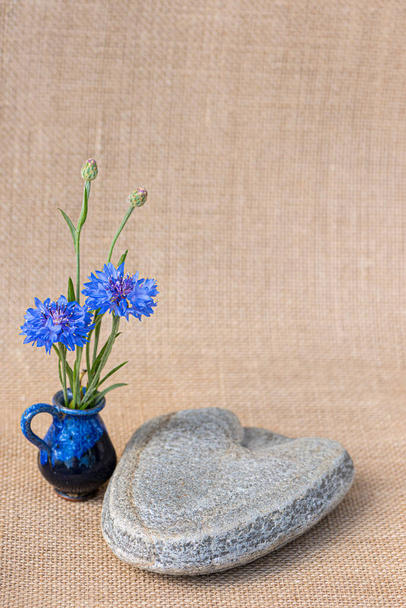 Bir taş kalp ve yanında küçük bir vazoda mavi çiçekler..  - Fotoğraf, Görsel