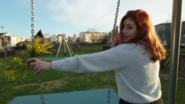 Fiatal gyönyörű vörös hajú lány élvezi a parkban játszik a swing  - Felvétel, videó