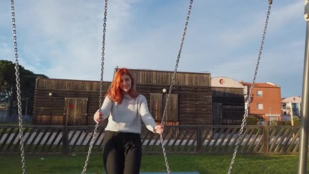 Giovane bella ragazza capelli rossi gode al parco a giocare con l'altalena - Filmati, video