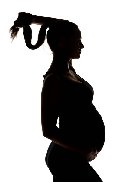 silhouette of a young pregnant woman holds her ponytail on a white background - Fotó, kép