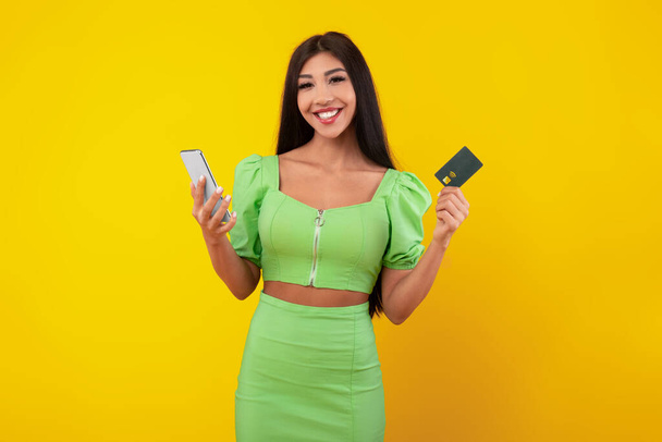 Mujer joven excitada sosteniendo tarjeta de crédito y teléfono celular - Foto, imagen