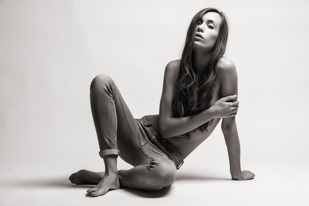 Fashion model sitting on a floor in a jeans barefoot on a white background - Foto, afbeelding