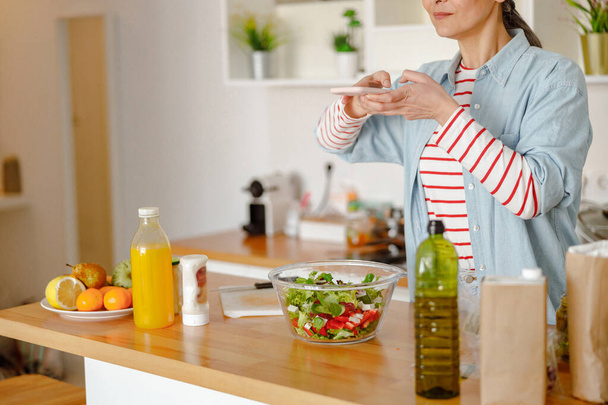 Mujer fotografiando ensalada fresca con smartphone en casa - Foto, imagen