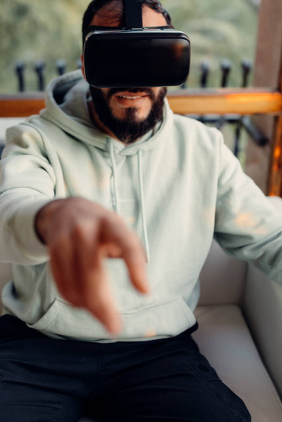 Bearded young man wearing VR glasses and pointing to the camera. Entertainment at home concept - Photo, image