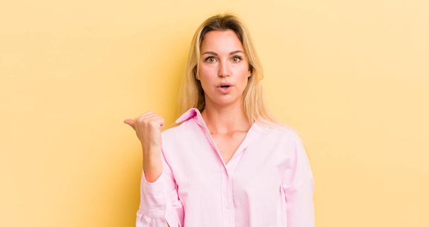 blonde caucasian woman looking astonished in disbelief, pointing at object on the side and saying wow, unbelievable - Фото, изображение