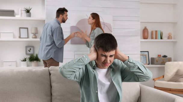 Unhappy teenage boy covering ears while his parents arguing on background. Problems at home - Fotoğraf, Görsel