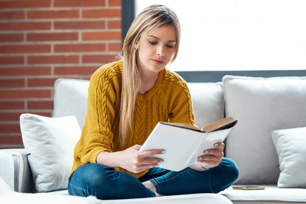 Shot of pretty young woman reading a book while sitting on sofa at home. - 写真・画像