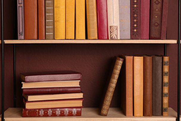 Shelves with different books on brown wall - Foto, imagen