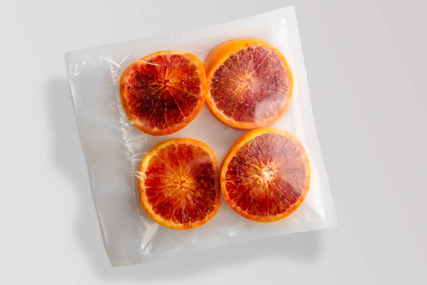 Quatre tranches d'oranges rouges dans un emballage sous vide scellé pour la cuisson sous vide isolé sur fond gris en vue du dessus - Photo, image