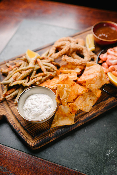 Seafood beer appetizers. Fried sprat, chips, shrimp, squid rings, lemon wedge, tomato sauce and tartar sauce - Foto, imagen