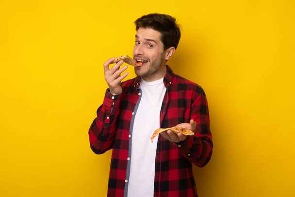 felice ragazzo tenendo fetta mordere pizza a studio - Foto, immagini
