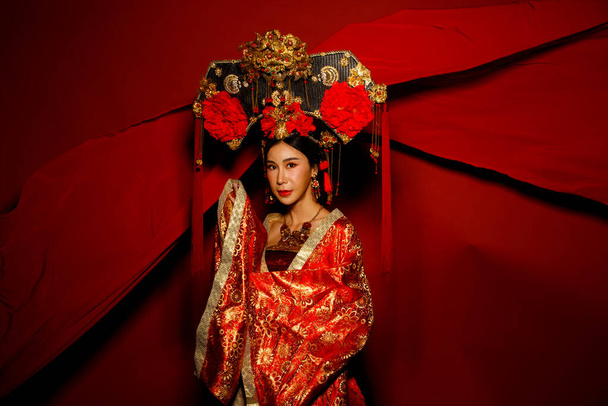 Dramatic Series vrouwelijke expressie gevoel emotioneel met stof fladderen in de lucht. Aziatische vrouw dragen China Royal keizerin traditionele kostuum met gouden lijn ontwerp jurk en hoofddeksel, rode achtergrond - Foto, afbeelding