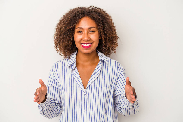 Jovem afro-americana com cabelo encaracolado isolado no fundo branco segurando algo com ambas as mãos, apresentação do produto. - Foto, Imagem