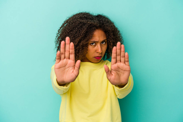 Nuori afrikkalainen amerikkalainen nainen kiharat hiukset eristetty sinisellä taustalla seisoo ojennettu käsi osoittaa stop-merkki, estää sinua. - Valokuva, kuva