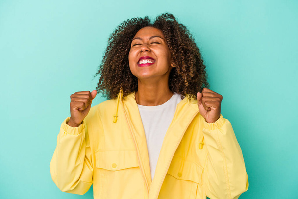 Mujer afroamericana joven con el pelo rizado aislado sobre fondo azul celebrando una victoria, pasión y entusiasmo, expresión feliz. - Foto, imagen