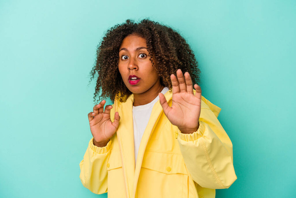 Young african american woman with curly hair isolated on blue background being shocked due to an imminent danger - Photo, Image