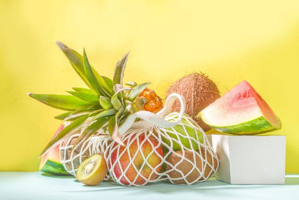 Sommer Obst einkaufen Hintergrund. Umweltfreundliche Einkaufstasche voller frischer tropischer Früchte, auf modernem, hellem Hintergrund mit Kopierraum in hartem Licht. Vitamin, gesundes Ernährungskonzept - Foto, Bild