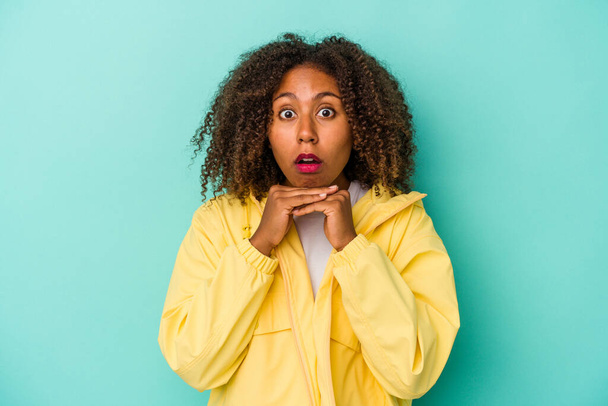 Young african american woman with curly hair isolated on blue background praying for luck, amazed and opening mouth looking to front. - Fotoğraf, Görsel