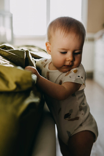 Крупный план портрета ребенка, стоящего рядом с кроватью, опирающегося на нее, дома. - Фото, изображение