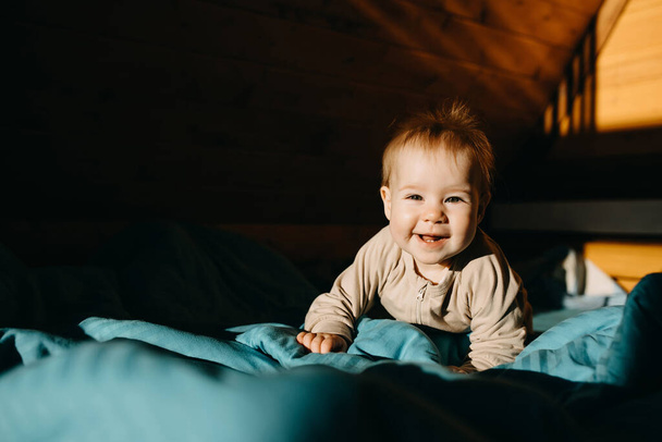 小さな9ヶ月の子供がベッドの上を這いカメラを見て笑って. - 写真・画像