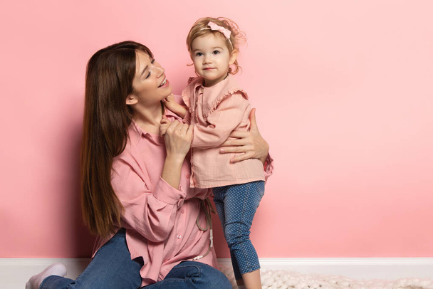 Support and care. Young woman and little girl, mother and daughter isolated on pink studio background. Mothers Day celebration. Concept of family, childhood, motherhood - Photo, image