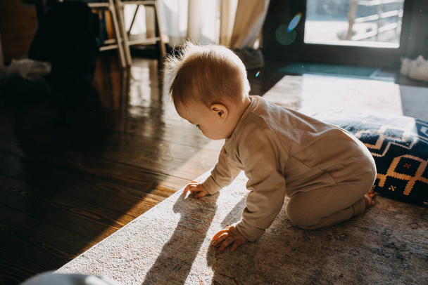 Little baby sitting on the floor at home in sun light, playing with carpet. - Photo, image