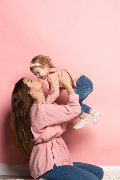 Portrait of young woman and little girl, mother and daughter isolated on pink studio background. Mothers Day celebration. Concept of family, childhood, motherhood - Zdjęcie, obraz