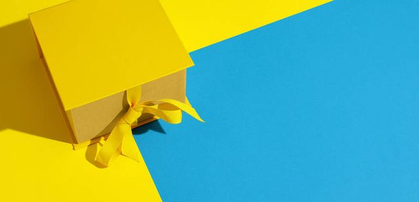 Heldere gele geschenkdoos met lint strik op gele en blauwe achtergrond bovenaanzicht kopieerruimte. Verjaardagscadeau, 8 maart, Moederdag, Valentijnsdag, Pasen of lente concept. - Foto, afbeelding