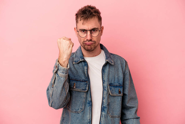 Young caucasian man isolated on pink background showing fist to camera, aggressive facial expression. - Foto, afbeelding