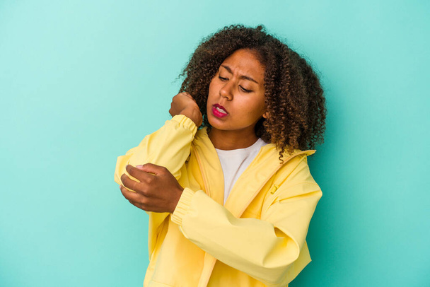 Jeune femme afro-américaine aux cheveux bouclés isolée sur fond bleu massant le coude, souffrant après un mauvais mouvement. - Photo, image