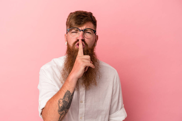 Fiatal fehér gyömbéres férfi hosszú szakállal elszigetelt rózsaszín háttérrel, aki titkot tart, vagy csendet kér. - Fotó, kép