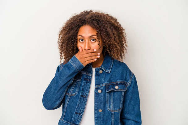 Νεαρή Αφροαμερικανή γυναίκα με σγουρά μαλλιά απομονωμένη σε λευκό φόντο που καλύπτει το στόμα με τα χέρια να φαίνονται ανήσυχα. - Φωτογραφία, εικόνα