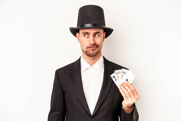 Молодий кавказький чарівник тримає чарівні картки ізольовані на білому тлі збентежені, відчуває сумнів і не впевненість
. - Фото, зображення