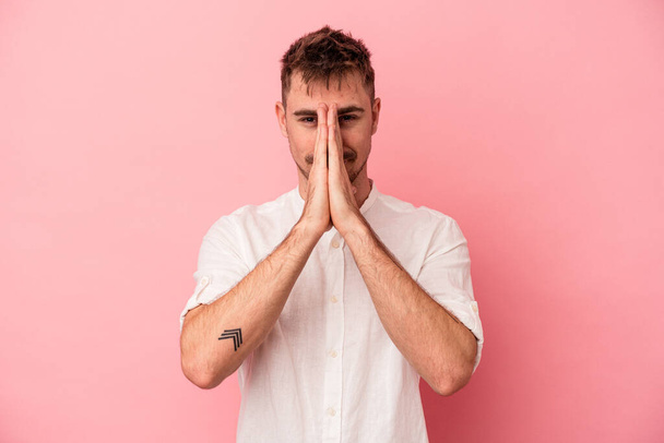 Молодий кавказький чоловік ізольований на рожевому тлі, тримаючи руки в молитві біля рота, відчуває себе впевнено
. - Фото, зображення