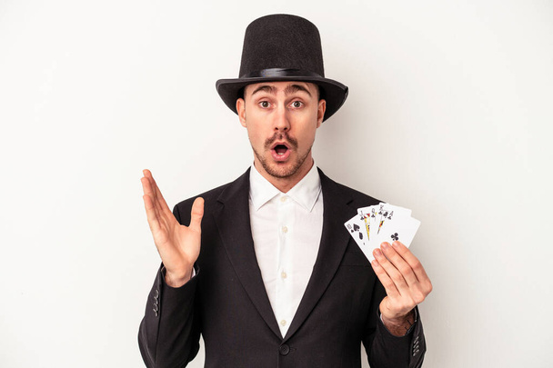 Молодий кавказький чарівник тримає чарівні карти ізольовані на білому тлі здивований і шокований
. - Фото, зображення
