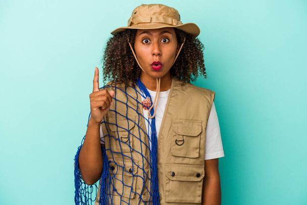 Νεαρή Αφροαμερικανίδα ψαράς που κρατά το δίχτυ απομονωμένο σε μπλε φόντο έχοντας κάποια σπουδαία ιδέα, έννοια της δημιουργικότητας. - Φωτογραφία, εικόνα