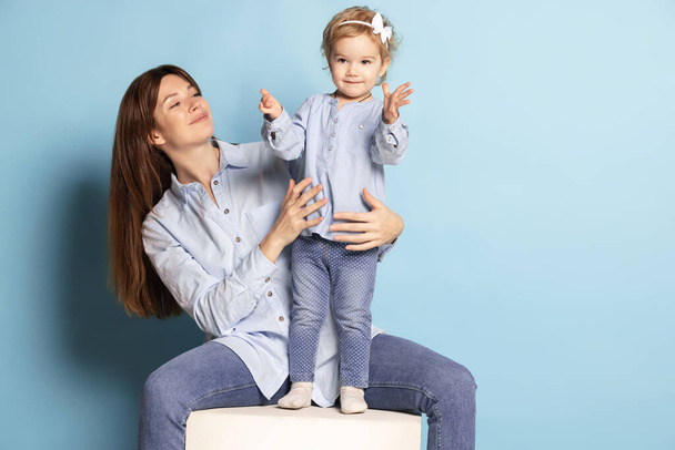 Studio shot of beautiful happy woman and little kid, mother and daughter isolated on blue background. Mothers Day celebration. Concept of family, childhood - Foto, Bild