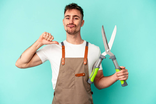 Young gardener caucasian man holding a scissors isolated on blue background feels proud and self confident, example to follow. - Photo, Image