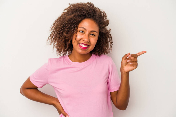 Mladá africká americká žena s kudrnaté vlasy izolované na bílém pozadí s veselým úsměvem ukazující ukazováčkem pryč. - Fotografie, Obrázek