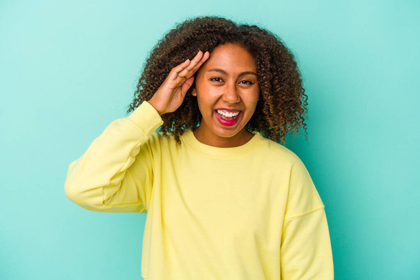 Fiatal afro-amerikai nő göndör haj elszigetelt kék háttér kiabál hangosan, tartja nyitva a szemét, és a kezét feszült. - Fotó, kép