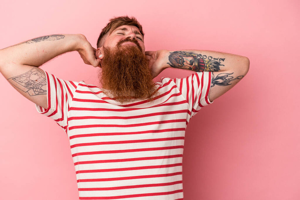 Jovem homem de gengibre caucasiano com longa barba isolada no fundo rosa sentindo-se confiante, com as mãos atrás da cabeça. - Foto, Imagem
