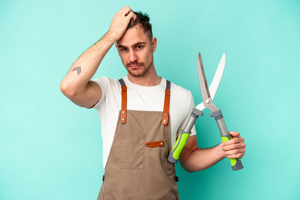 Young gardener caucasian man holding a scissors isolated on blue background being shocked, she has remembered important meeting. - Photo, Image